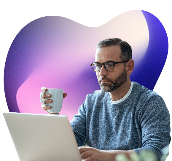 A man holds a cup in one hand while reading something on a laptop screen