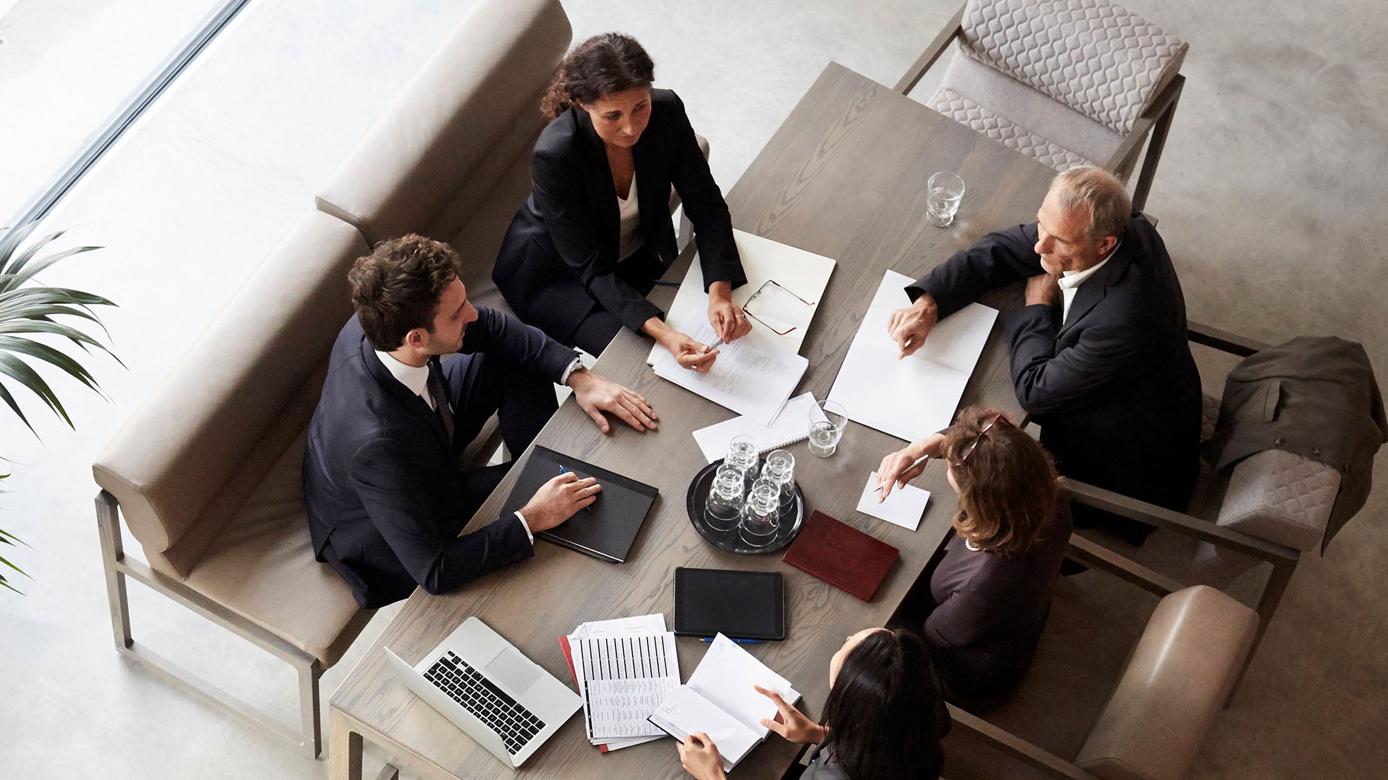 A group of smartly suited people meet around a table